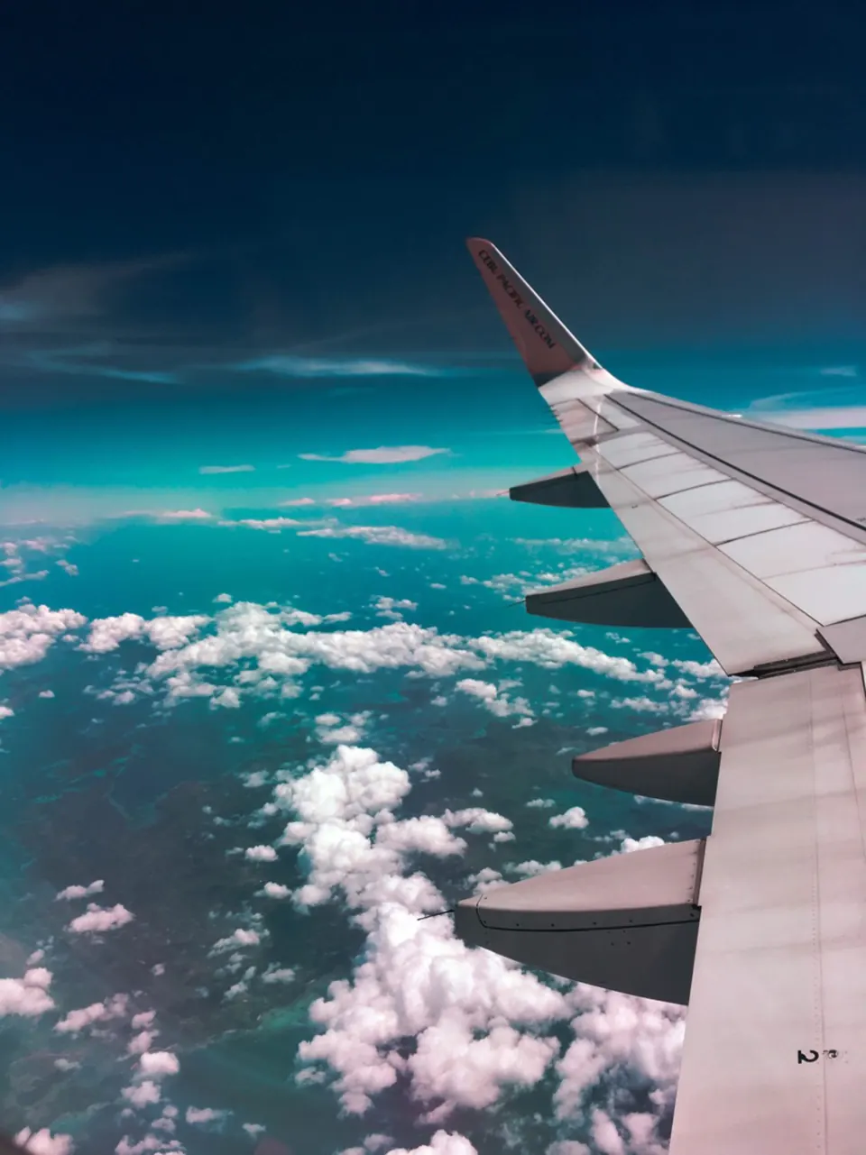 Aircraft wing above scattered clouds over a turquoise sea