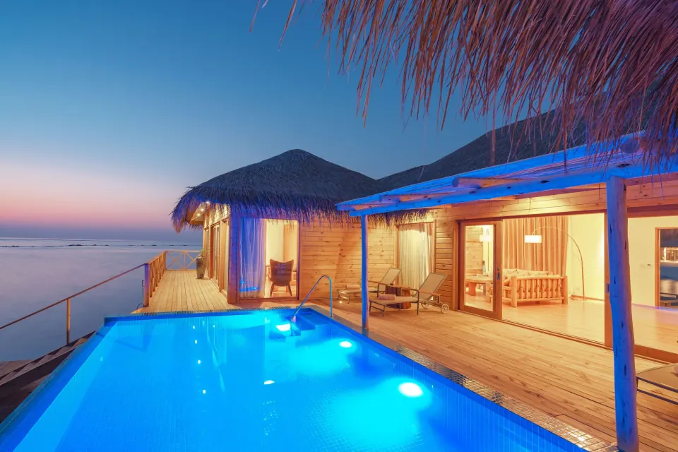 Overwater villa with a private infinity pool glowing at dusk in the Maldives