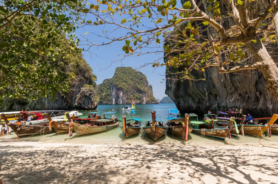 Longtail boats lined up on a Krabi beach below limestone cliffs