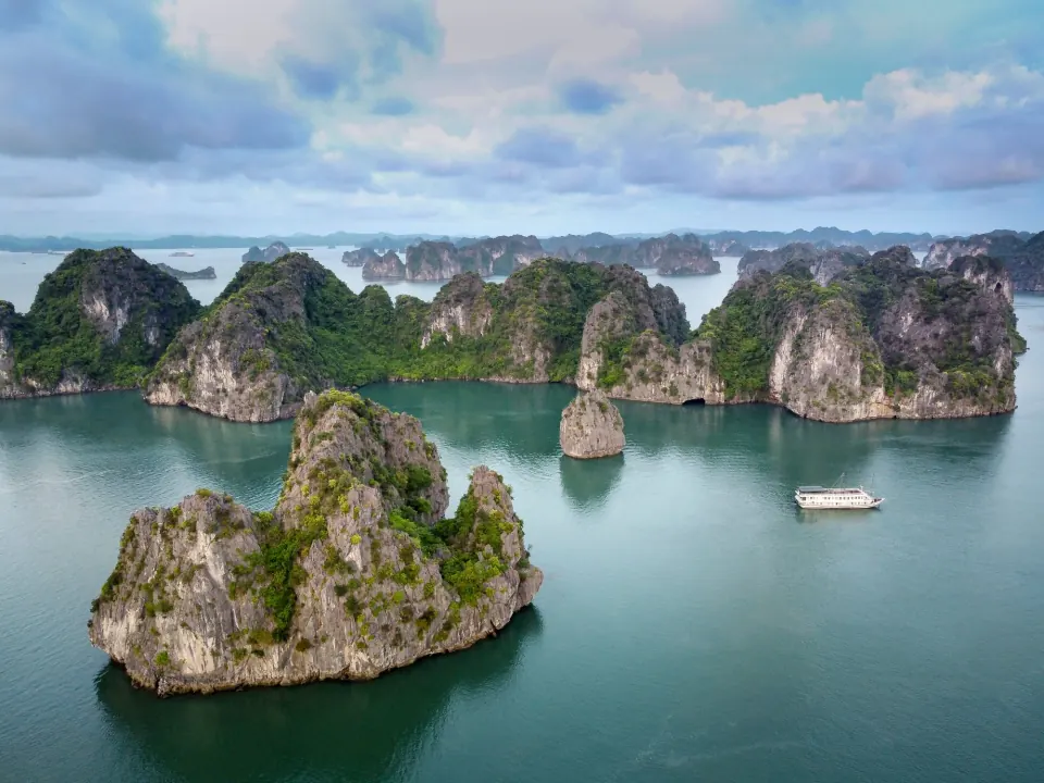 Limestone islands and a cruise boat on the calm water of Ha Long Bay