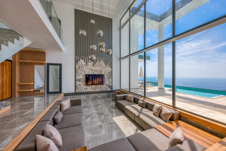 Bright living room of a luxury villa with floor to ceiling windows onto a sea view pool