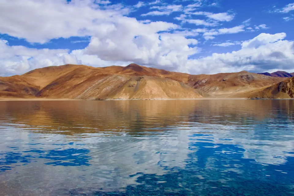 Pangong Tso lake reflecting golden hills and a blue sky in Ladakh