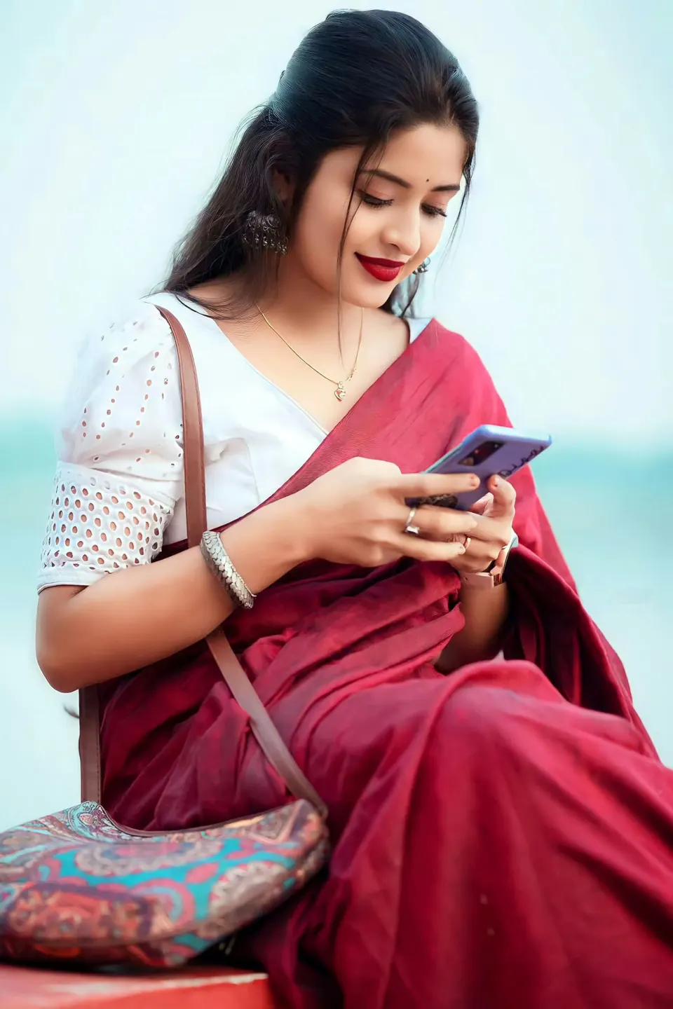 Smiling Indian woman in a red saree reading on her phone