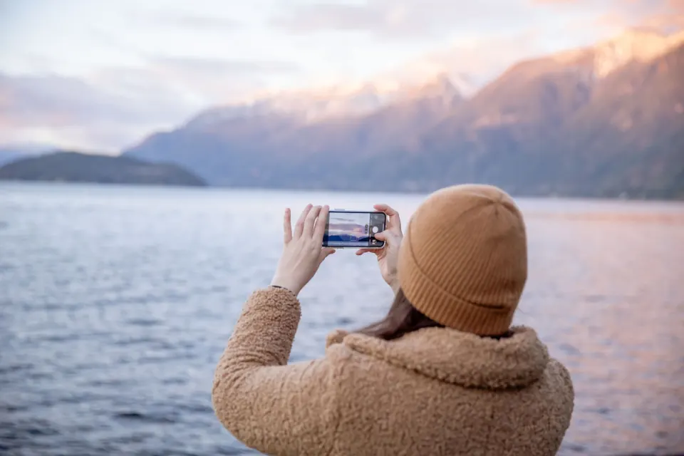 Traveller photographing mountains across the water with her phone